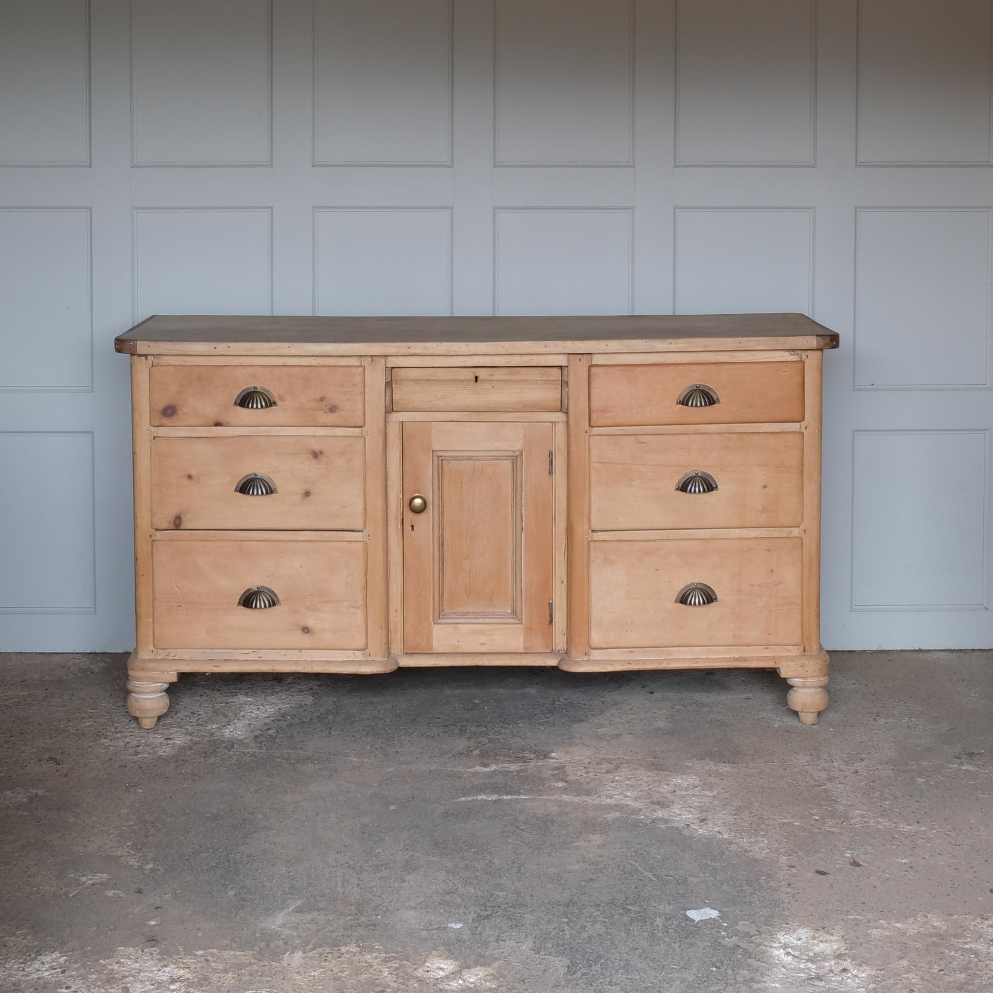 A large oak sideboard with, presumably late 19th / early 20th Century, comprising three drawers on each side with scallop cup handles, and a central drawer over a hinged cupboard door, raised on four turned bun feet. In very good, solid condition. Perfect for a kitchen or entrance hallway.