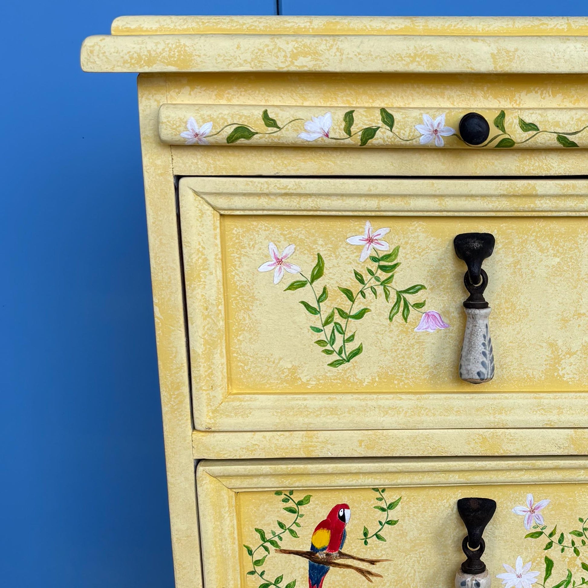 A stunning, unique matching pair of hand-painted chests of drawers, with brushing slides over three drawers. Finished in a fetching patinated yellow and decorated with exotic animals and Flora, in very good condition. Ideal for a children's bedroom or to liven up a sitting room. A unique pair in collaboration with Bunny Howe.