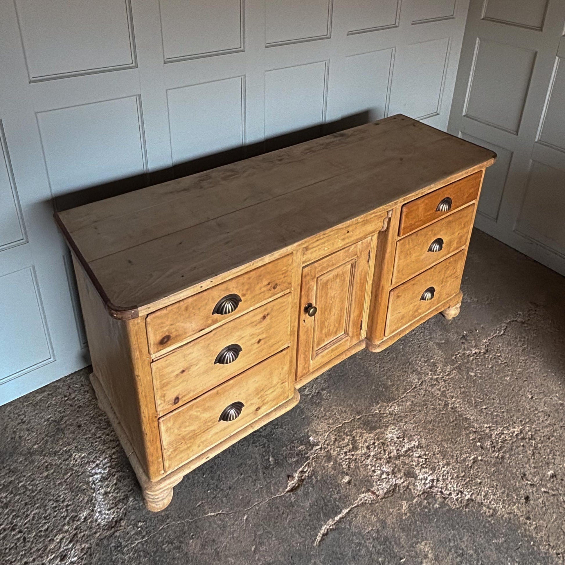 A large oak sideboard with, presumably late 19th / early 20th Century, comprising three drawers on each side with scallop cup handles, and a central drawer over a hinged cupboard door, raised on four turned bun feet. In very good, solid condition. Perfect for a kitchen or entrance hallway.